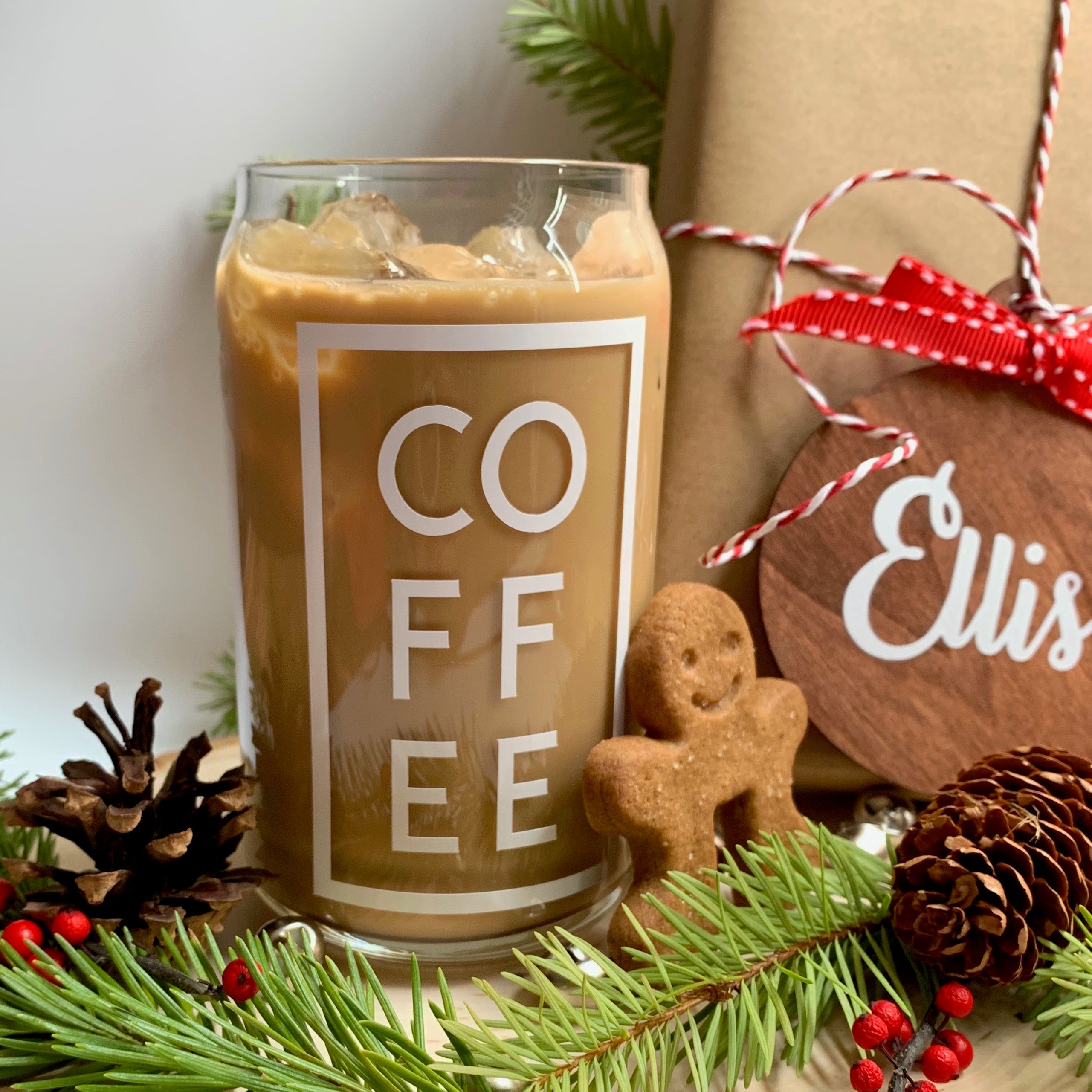 Clear coffee can glass, beer can glass, with white COFFEE design. The word on the glass is COFFEE there is a long rectangular box around the letters.It is filled with iced coffee and ice. Pictured is a wood ornament with a red ribbon on a brown gift box, there are pinecones, red berries, Christmas tree branch and a gingerbread man. This perfect for cold drinks like iced coffee, iced tea, or any other cold beverage. Gift for him, for her, gift for them. gift for you